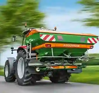 Grün-orangener Düngerstreuer an einem Traktor montiert